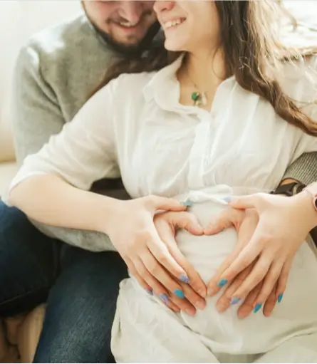 a pregnant woman and her husband holding her belly with a heart symbol in their hands