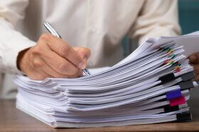 a person writing with a pen on a stack of papers